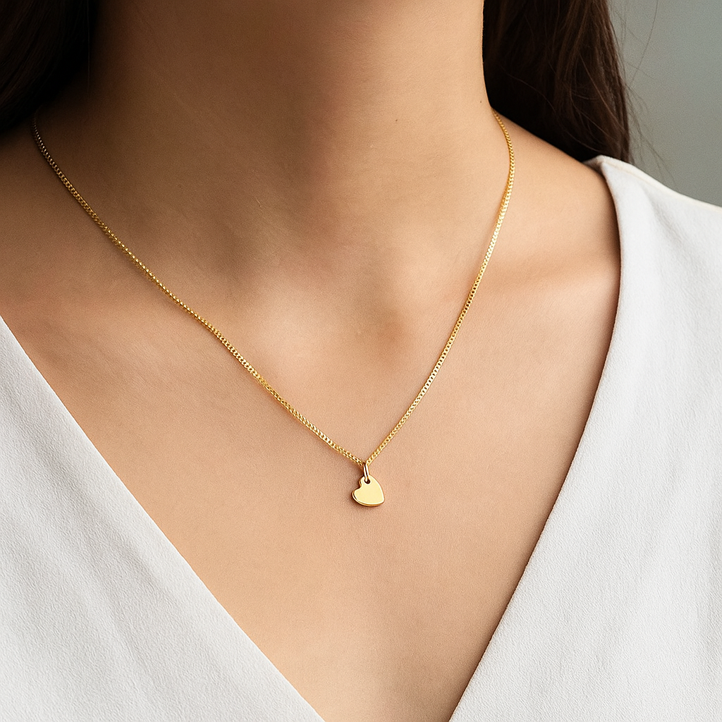 Gold necklace with a heart pendant worn by a person in a white top.