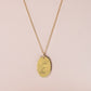 Gra go Deo engraved on gold oval disc on a plain pink background