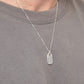 Man wearing a gray sweater with a silver necklace featuring a dog tag.