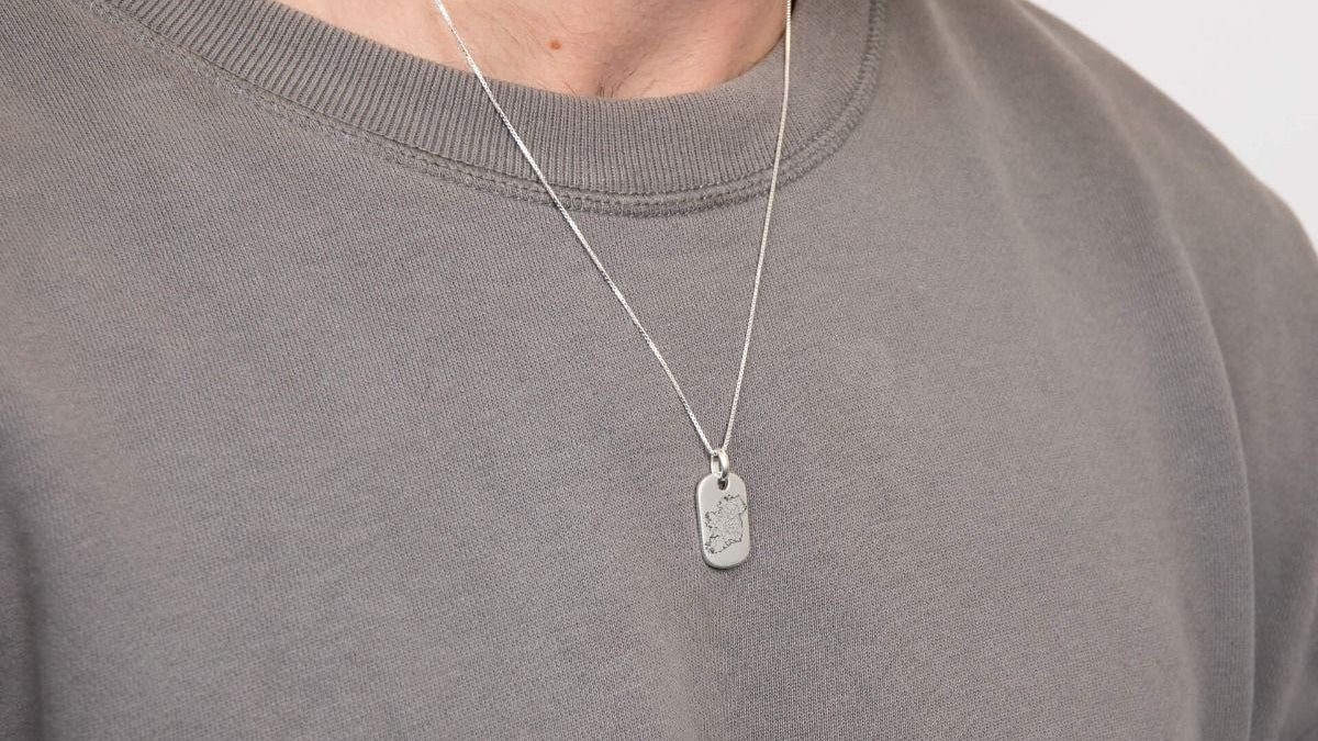 Man wearing a gray sweater with a silver necklace featuring a dog tag.